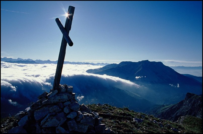 Photo : La petite croix, deux bouts de bois, qui marque le sommet de la Tte de Garnesier, en Dvoluy. Nuages bas sur l'intrieur du massif, et soleil au dessus. 
