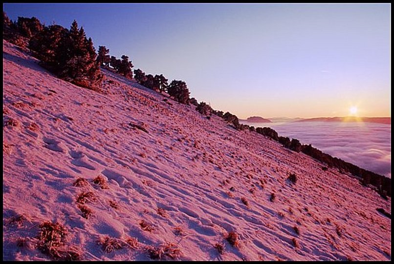 Photo : Soleil couchant au dessus du Vercors, mer de nuages sur la plaine de Grenoble et pentes peu enneiges de Chamechaude, en Chartreuse. 
